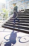 Businessman in suit and helmet carrying bicycle down urban stairs