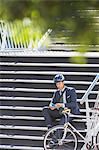 Businessman with helmet and bicycle texting with cell phone on urban stairs