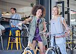 Portrait smiling women on bicycles outside cafe