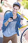 Young man with helmet carrying bicycle and texting on cell phone