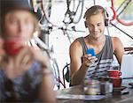 Young man with headphones and laptop texting with cell phone in cafe