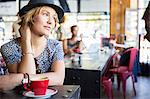 Pensive woman in hat with coffee looking away in cafe