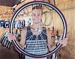 Portrait smiling young man holding bicycle wheel in bicycle shop