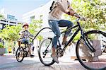 Son in helmet riding tandem bicycle with mother in urban park