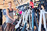 Portrait smiling young man leaning on rack in bicycle shop