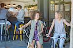 Smiling women on bicycles outside cafe patio