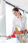 Businesswoman talking on cell phone working at computer in office