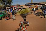 Back view of lady wearing colorful dress, carrying basket with grass brushes on her head to market, Bobo-Dioulasso, Burkino Faso