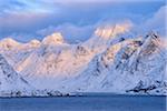 View from the Spellmannsbukta to Kunna Island and Flakstadoya. Mountains covered with snow in winter, sunset. Kunna Island, Flakstadoy, Lofoten, Norway, Scandinavia.