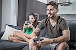 Young couple on sofa using smartphone and gaming control