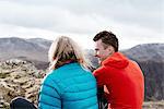 Young couple sitting on hilltop, rear view, Keswick, Lake District, Cumbria, United Kingdom