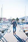 Young man talking on smartphone whilst walking on lake pier