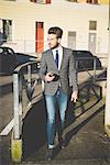 Stylish young man with smartphone walking on sidewalk