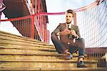 Stylish young man sitting on footbridge stairs with smartphone