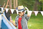 Boy eating ice lolly whilst adjusting trilby hat in garden