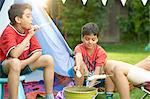 Girl and brothers toasting marshmallows in front of homemade tent in garden