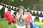 Girl covering her eyes for hide and seek with brothers in garden