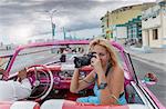 Young woman photographing from a vintage car on the Havana' Malecon, Cuba