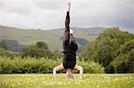 Mature woman practicing yoga standing on head with leg raised in field