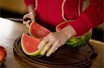 Cropped view of mature woman slicing watermelon in kitchen