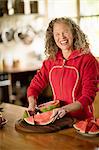 Portrait of mature woman slicing watermelon in kitchen