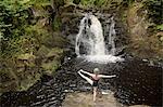 Rear view of mature woman practicing yoga in front of waterfall