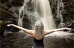 Rear view of mature woman practicing yoga pose in front of waterfall