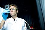 Male scientist holding up and scrutinizing specimen in lab cleanroom