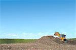 Digger on mound burying waste on landfill site