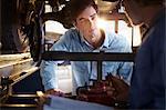 Mechanic and customer talking under car in auto repair shop