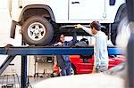 Mechanic under car talking to customer in auto repair shop