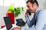 Businessman talking over the phone while typing on laptop at same time. Side profile