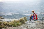 Woman tourist sitting on edge of rock and looking at valley below