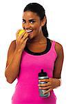 Young female athlete eating green apple and holding sipper bottle