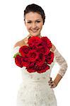 Beautiful bride with one hand on waist displaying a bunch of red roses