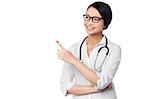 Young smiling casual female doctor looking and pointing away