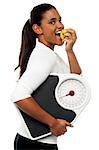 Fitness instructor eating fresh green apple and holding weight scale.