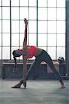 A strong, muscular woman is doing the extended triangle pose in yoga in a city loft gym.