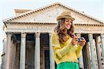 A brunette woman smiles, looking down at her digital camera, checking her photos. Behind her, the Pantheon in Rome on a warm summer's day.