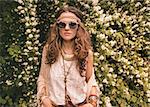 Longhaired hippy-looking young lady in knitted shawl and white blouse standing among flowers