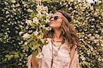 Longhaired hippy-looking young lady in knitted shawl and white blouse enjoying flowers fragrance