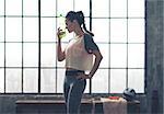 Standing in profile, a woman cools her forehead off with her bottle of ice-cold water. Her eyes are closed, and it feels so soothing after a hot workout.