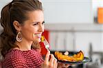 A closeup profile shot of a happy, elegant woman as she looks into the distance, smiling. Her fork is poised, ready for her to take a bite. On her plate, roasted pumpkin.