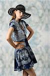 charming female posing in fashion shoot with black hat and blue printed top and skirt. Looking in camera