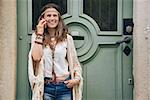 Laughing hippie brunette woman in bohemian clothes woman standing outdoors against wooden door in old town and talking cell phone