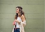 Happy trendy hipster woman with mobile phone in jeans shorts, knitted shawl and white blouse standing outside buildings in street