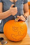 Close up on woman carving a pumpkin Jack-O-Lantern for Halloween party in kitchen. Traditional autumn holiday