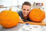 Funny young brunette woman in kitchen creating big orange pumpkins Jack-O-Lantern on Halloween party. Traditional autumn holiday