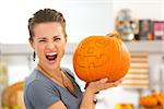 Portrait of young woman scaring with big Halloween pumpkin Jack-O-Lantern. Traditional autumn holiday