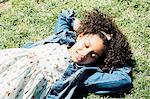 High angle view of girl lying on back on grass, hands behind head, eyes closed